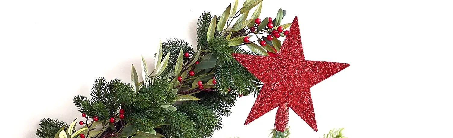 Rød julestjerne med glimmer vist på toppen af et kunstigt juletræ
