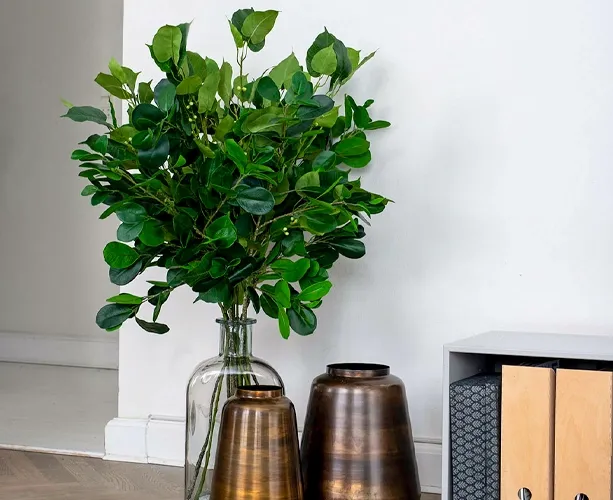 Kunstige hellig figen grene sat i en vase der er udformet som en karaffel