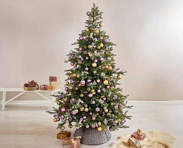 kunstigt grønt juletræ med julepynt i guld og lilla nuancer, med fin flettet juletræsfod omkring